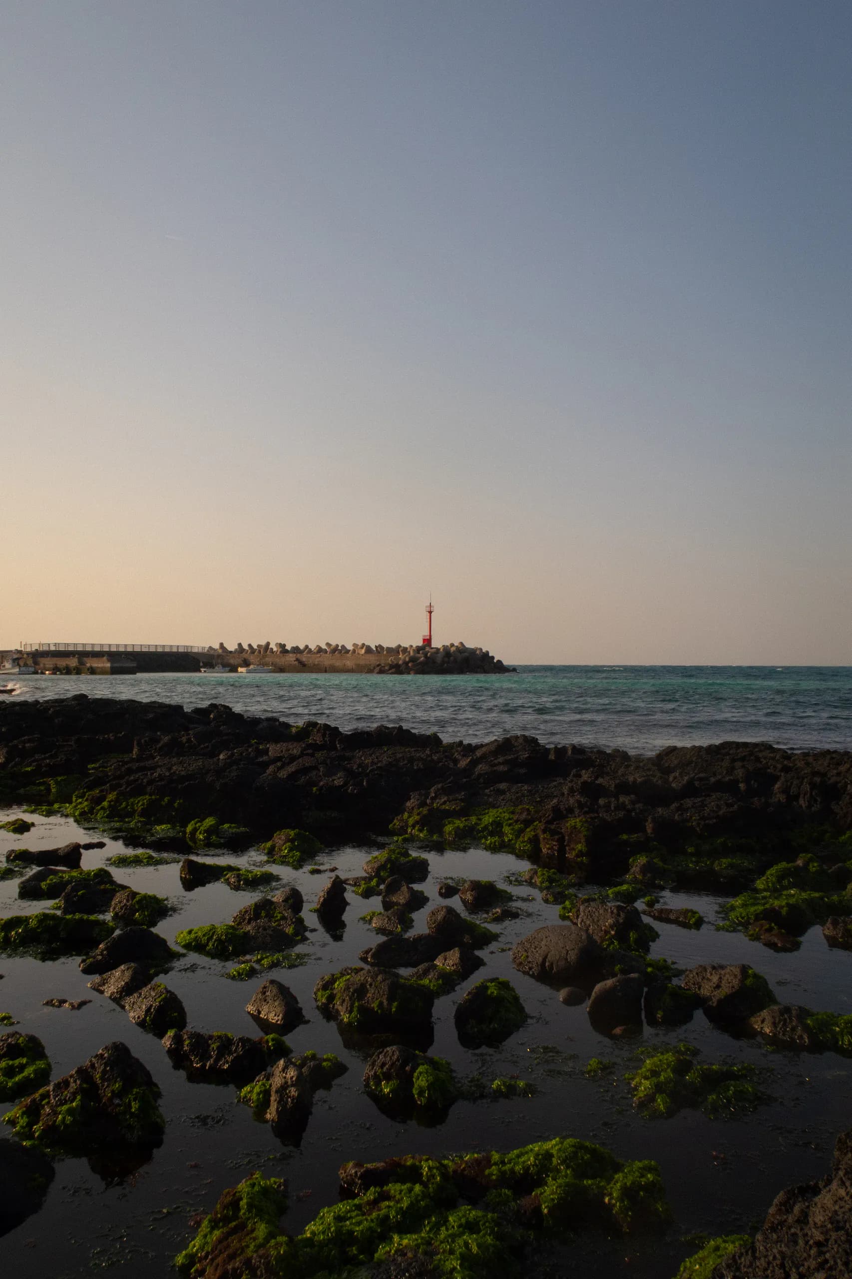 Pyoseon-area lighthouse at sunset over basalt tide pools