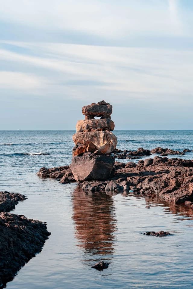 A stacked stone cairn on the basalt shore at dusk