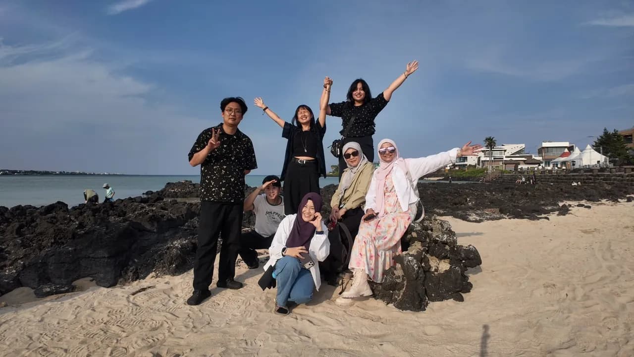 The cohort posing on a sandy Jeju beach under a bright blue sky