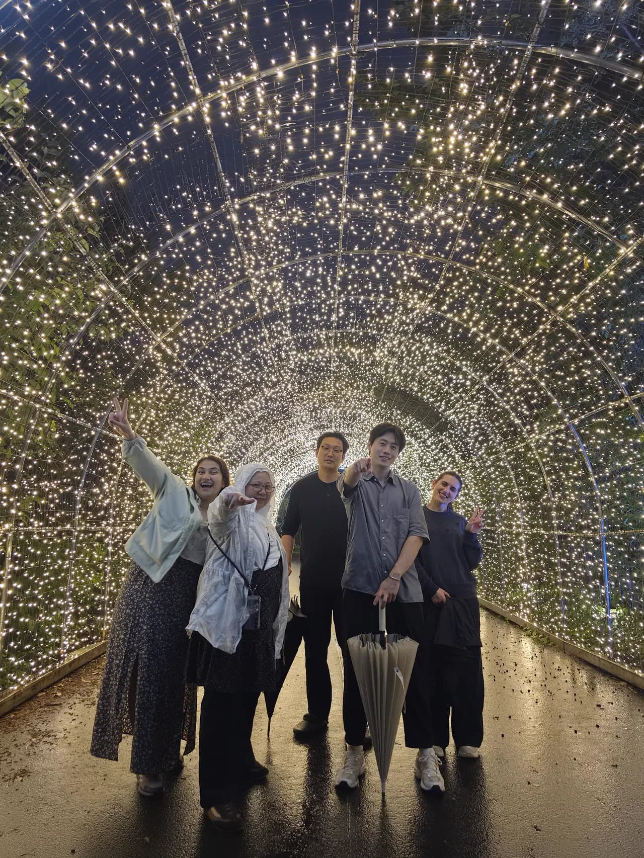 The cohort together inside a glowing fairy-light tunnel at night